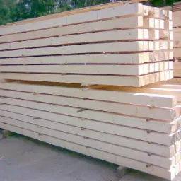 Stos jasnego, świeżo obrobionego drewna budowlanego, ułożonego warstwami na placu składowym, widoczne deski, łaty i krokwie.