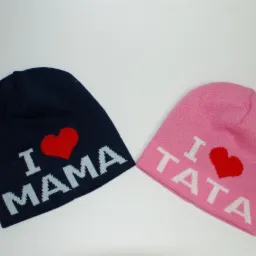 Dwie dziergane czapki: granatowa z napisem 'I ❤️ MAMA' i różowa z napisem 'I ❤️ TATA', leżące na białym tle.
