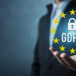 Mężczyzna w garniturze trzyma w dłoni symbol GDPR otoczony gwiazdami na niebieskim tle.