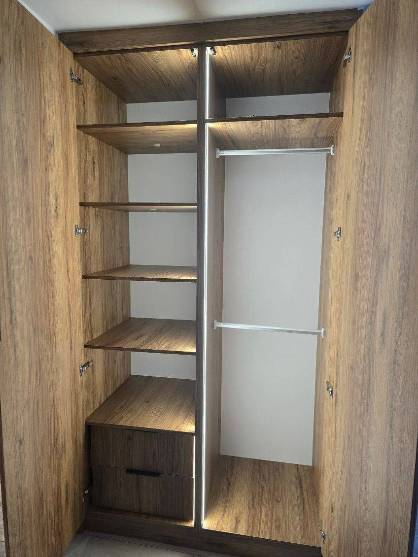 Otwarta szafa wnękowa z oświetleniem LED, półkami z forniru imitującego drewno i szufladą na dole.