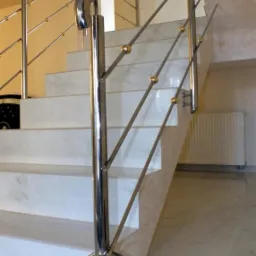 Nowoczesne schody z marmurowymi stopniami i balustradą ze stali nierdzewnej z dekoracyjnymi złotymi kulami. Widok z dołu, podkreślający detale wykończenia.