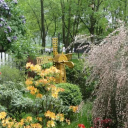 Urokliwy ogród prywatny z kwitnącymi krzewami, kolorowymi azaliami i dekoracyjnym, żółtym wiatrakiem w tle.