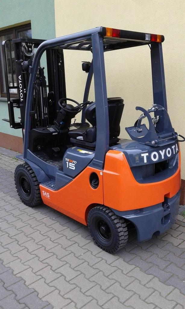 Pomarańczowo-szary wózek widłowy Toyota 15, stojący na kostce brukowej przed budynkiem.