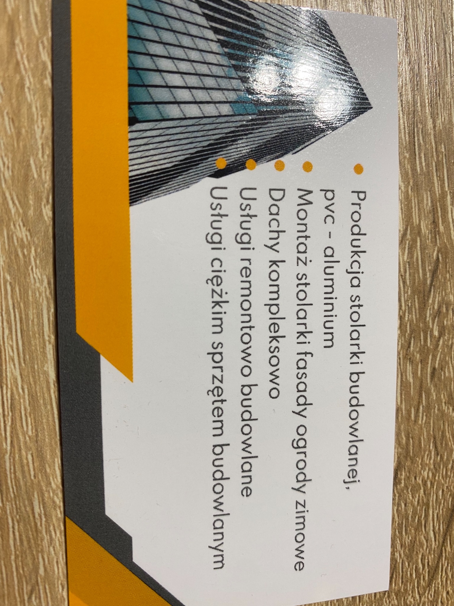 Wizytówka firmy budowlanej z ofertą produkcji stolarki, montażu fasad, dachów i usług remontowych.