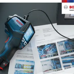 Kamera termowizyjna Bosch GIS 1000 C leżąca na dokumentach z wynikami pomiarów termowizyjnych, widoczne ekrany z temperaturami i obrazami z kamery.