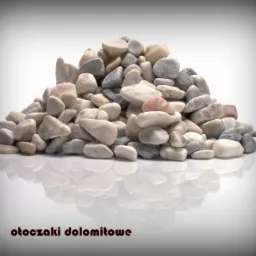 Stos otoczaków dolomitowych w odcieniach szarości i bieli, z delikatnym różowym akcentem, ułożonych na błyszczącej powierzchni z wyraźnym odbiciem, na białym tle z winietą.