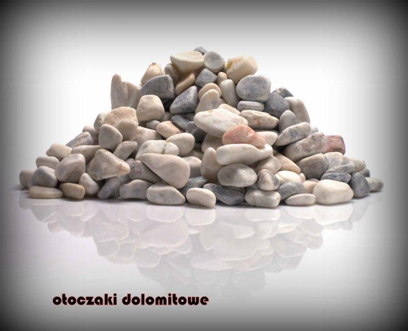 Stos otoczaków dolomitowych w odcieniach szarości i bieli, z delikatnym różowym akcentem, ułożonych na błyszczącej powierzchni z wyraźnym odbiciem, na białym tle z winietą.