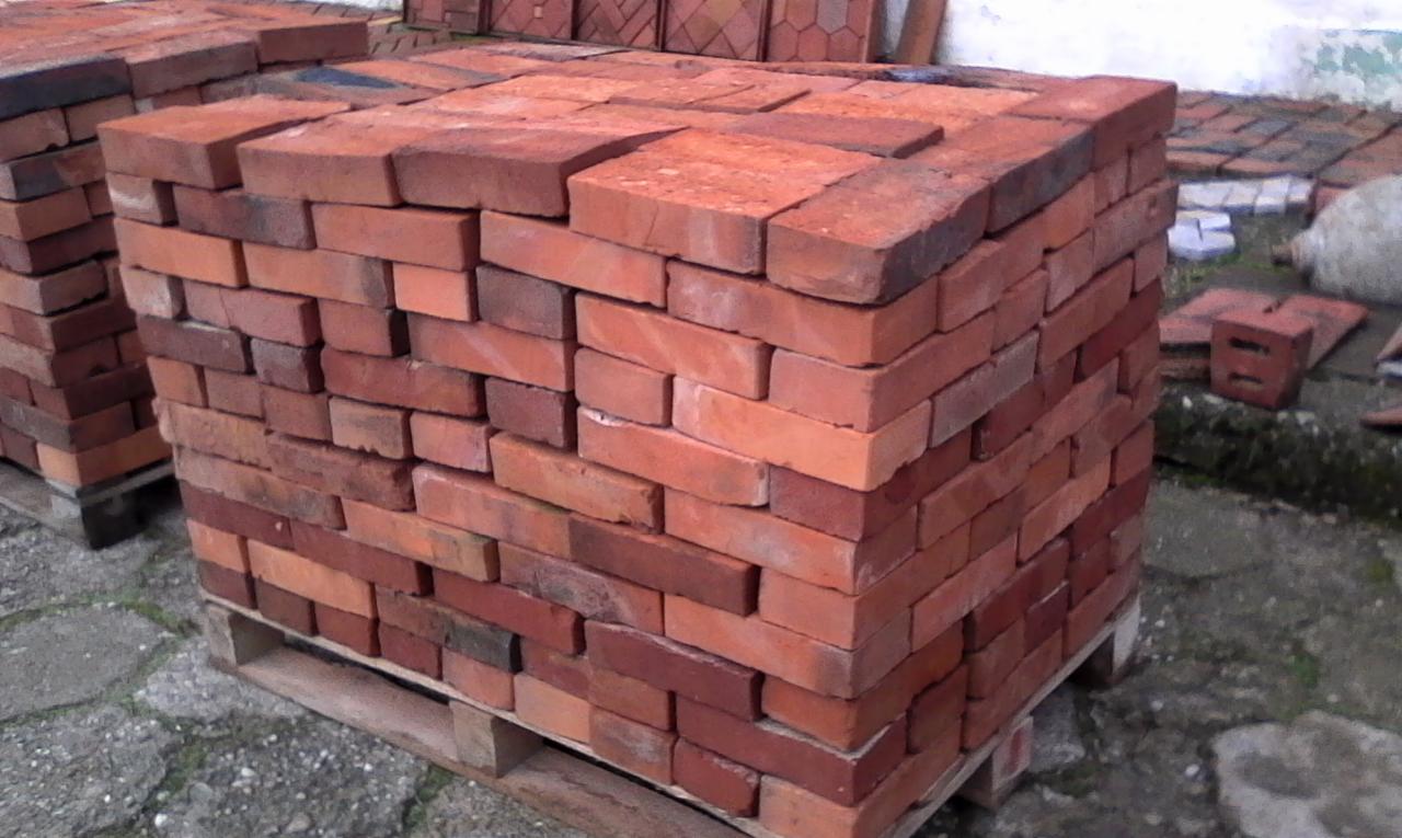 Paleta z cegłami w odcieniach czerwieni i pomarańczu, ułożonymi równo w stos, widoczne ślady użytkowania palety i zabrudzenia cegieł.