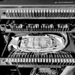 Czarno-białe zbliżenie panelu krosowniczego światłowodowego z widocznymi złączami oznaczonymi numerami, okablowaniem i tacką światłowodową wewnątrz obudowy.