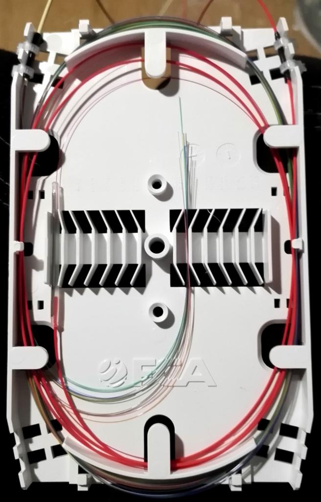 Rozdzielnica światłowodowa z uporządkowanymi kablami w kolorach czerwonym, zielonym i niebieskim, widoczne uchwyty i oznaczenia producenta.