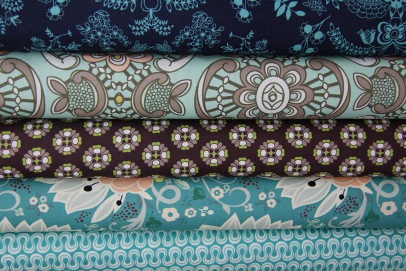 Stos bawełnianych tkanin Art Gallery Fabrics z różnorodnymi, kolorowymi wzorami kwiatowymi i geometrycznymi, ułożonych jedna na drugiej.