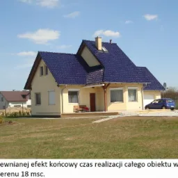 Gotowy dom jednorodzinny z ciemnoniebieskim dachem i jasną elewacją, z zagospodarowanym terenem, widoczny samochód i motocykl na podjeździe, mały domek dla dzieci na trawniku.