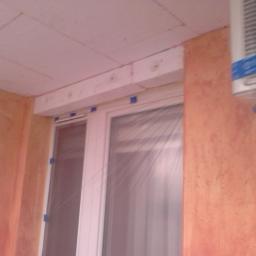 MAX WOJCIECH BARTOS - Fragment balkonu z widoczną nową zabudową okienną, ociepleniem sufitu i ścian wykończonych tynkiem strukturalnym w odcieniach pomarańczy, klimatyzator na ścianie.