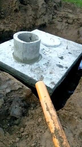 Betonowa studzienka kanalizacyjna z pokrywą, osadzona w wykopie, widoczna rura odpływowa