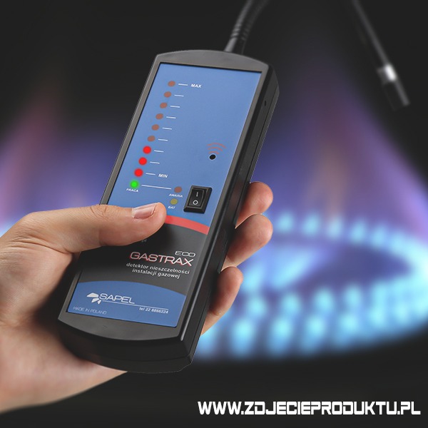 Dłoń trzyma detektor nieszczelności gazu GASTRAX ECO firmy SAPEL, z widocznym panelem z diodami LED wskazującymi poziom stężenia gazu oraz płomień gazu w tle.