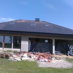 Ciesielstwo-Dekarstwo - Dom w trakcie wymiany dachu z widocznym starym pokryciem dachowym na trawniku, nowe dachówki na dachu, okna dachowe i częściowo ocieplone ściany zewnętrzne.