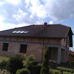 Ciesielstwo-Dekarstwo - Dom w trakcie budowy z nowym dachem z brązowej dachówki ceramicznej i oknami dachowymi, widoczne rusztowanie i elementy wykończeniowe.