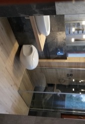 Nowoczesna aranżacja łazienki w Chorzowie z białymi, owalnymi umywalkami wiszącymi na drewnianych półkach, na tle ciemnych, grafitowych płytek i jasnej podłogi imitującej drewno.