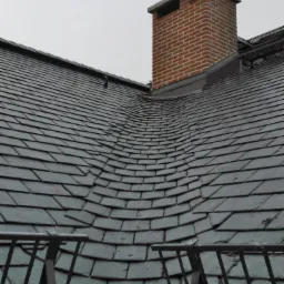 Dach pokryty łupkiem z widocznym kominem z cegły i barierkami na dachu, wykonany w pochmurny dzień.