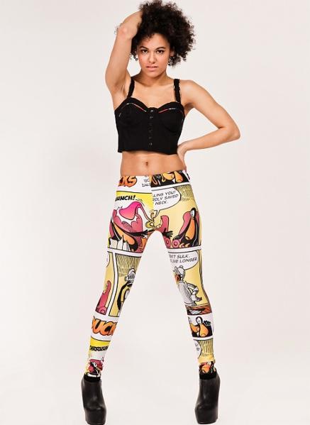 Kobieta w czarnym topie i legginsach z motywem komiksowym na białym tle, pozująca z ręką na biodrze, eksponując unikalny wzór graficzny na odzieży.