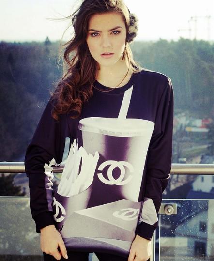 Kobieta w czarnej bluzie z nadrukiem kubka na napój i frytek na tle miejskiego krajobrazu.