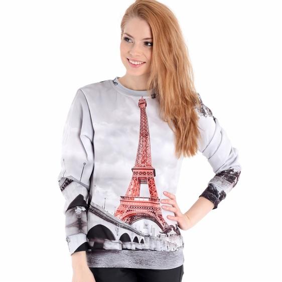 Kobieta prezentuje szarą bluzę z długim rękawem, na której nadrukowany jest widok Wieży Eiffla i mostu.