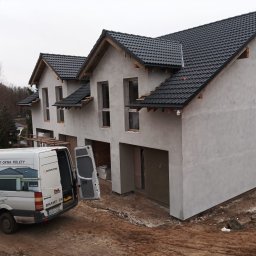 HMB MIKRON - Surowy stan trzypiętrowego domu szeregowego z otworami okiennymi i garażowymi, na pierwszym planie samochód dostawczy z reklamą bram, okien i rolet firmy Krispol.