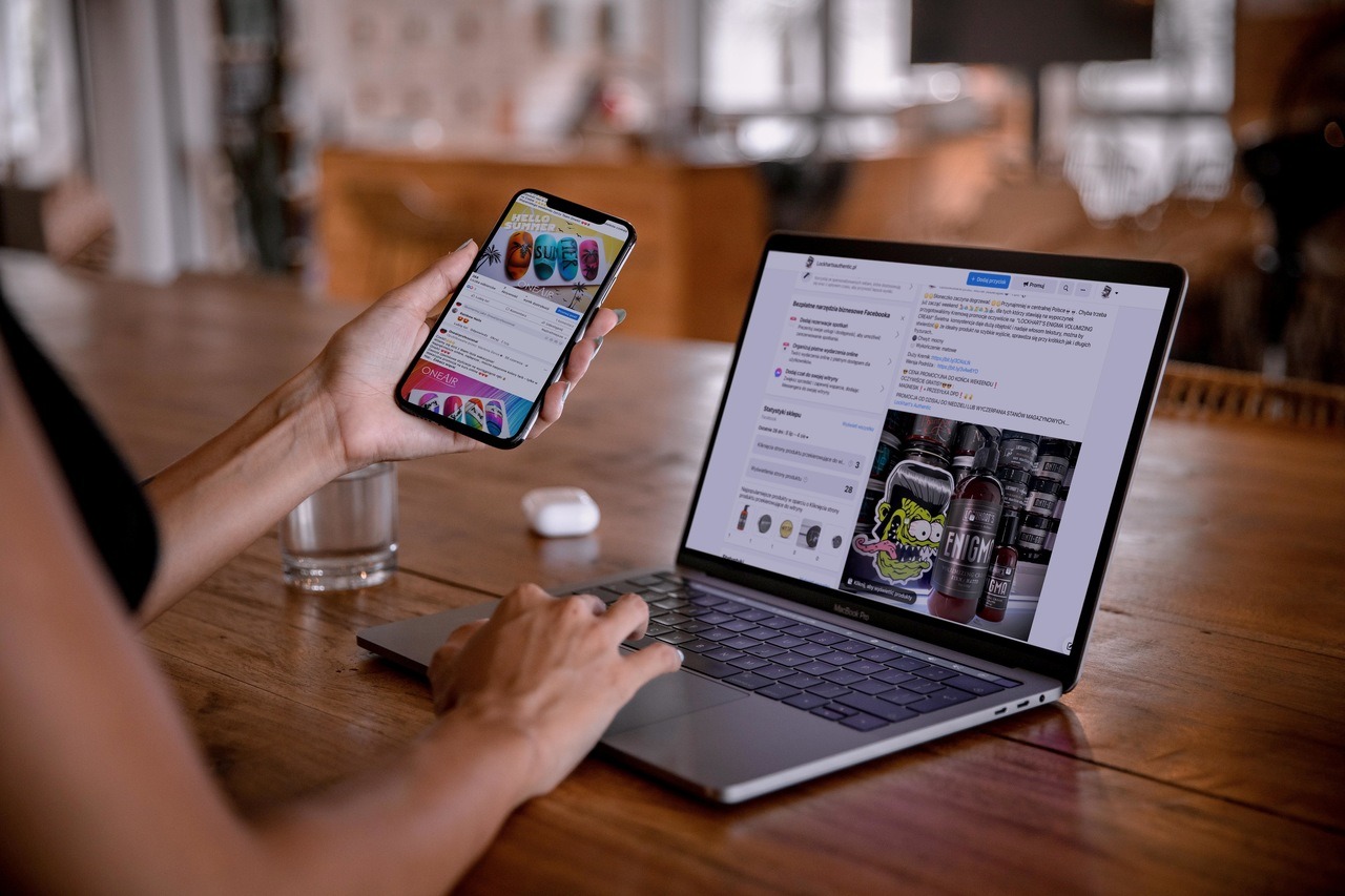 Osoba używa laptopa i smartfona do przeglądania Facebooka, gdzie widoczne są reklamy produktów kosmetycznych i fryzjerskich. Na ekranie laptopa widoczne są statystyki sklepu i reklamy z produktami...