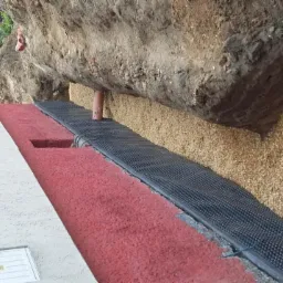 Fundament budynku z izolacją, folią kubełkową i drenażem z otoczaków, widoczne rury drenażowe odprowadzające wodę.