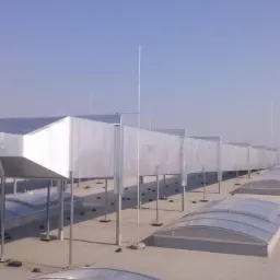 Długi, srebrny system wentylacyjny na płaskim dachu z świetlikami kopułowymi, widziany z perspektywy ukośnej pod słońcem.