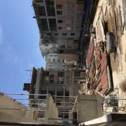 Grand World Company Sp.zo.o. - Wznoszenie wielopiętrowego budynku z cegły i betonu, widok z góry na plac budowy z pracującymi robotnikami, dźwigiem i materiałami budowlanymi.