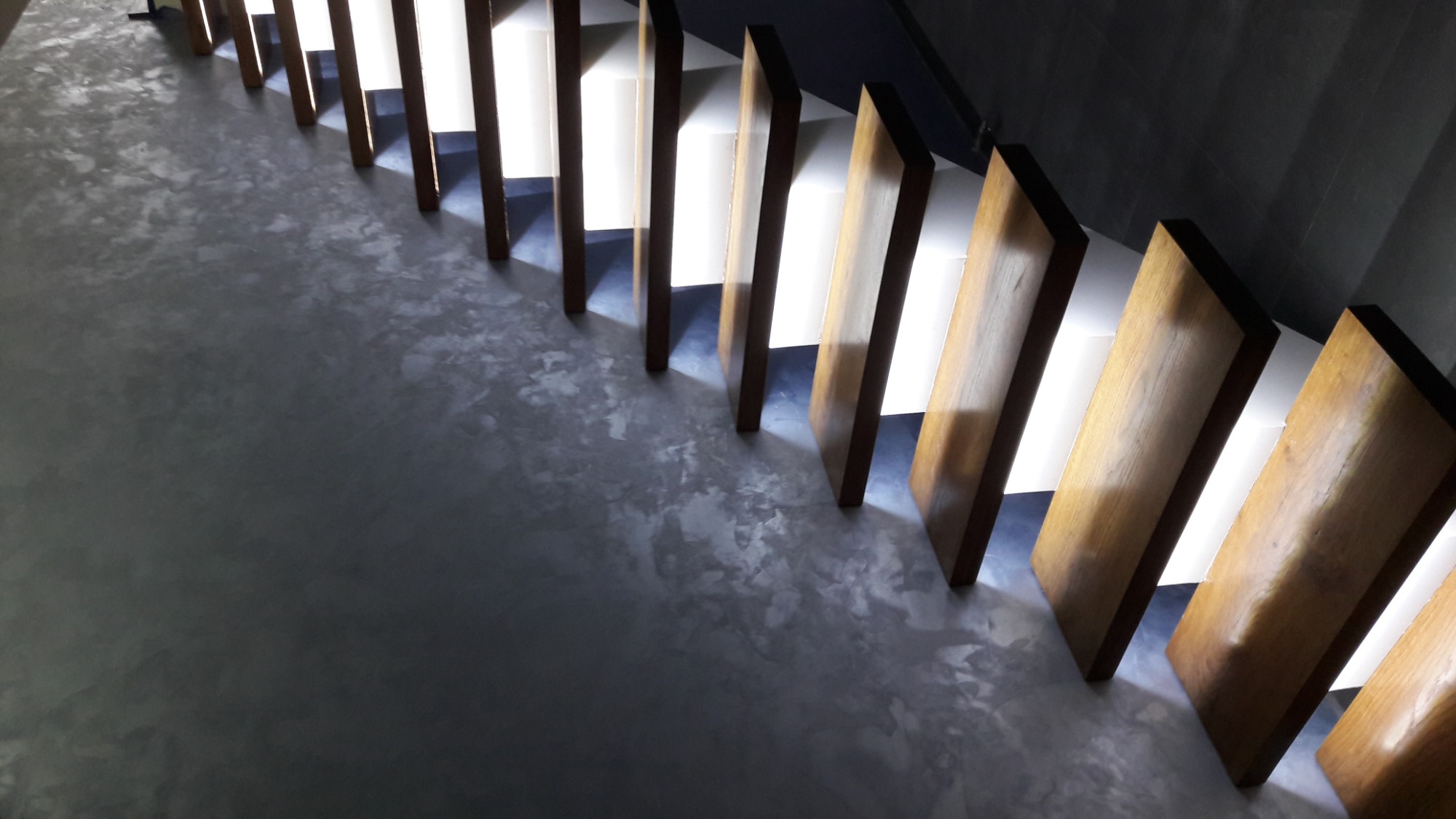 Nowoczesne schody z drewnianymi stopniami i podświetleniem, wykończone szarą, dekoracyjną posadzką.