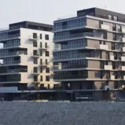 Dwa nowoczesne, wielopiętrowe budynki mieszkalne z balkonami, o różnych odcieniach szarości i bieli, widoczne z perspektywy lekko od dołu, na tle błękitnego nieba i fragmentów zieleni.