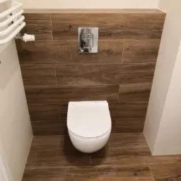 Podwieszana toaleta z drewnopodobną zabudową i chromowanym przyciskiem spłukującym, widok z przodu.