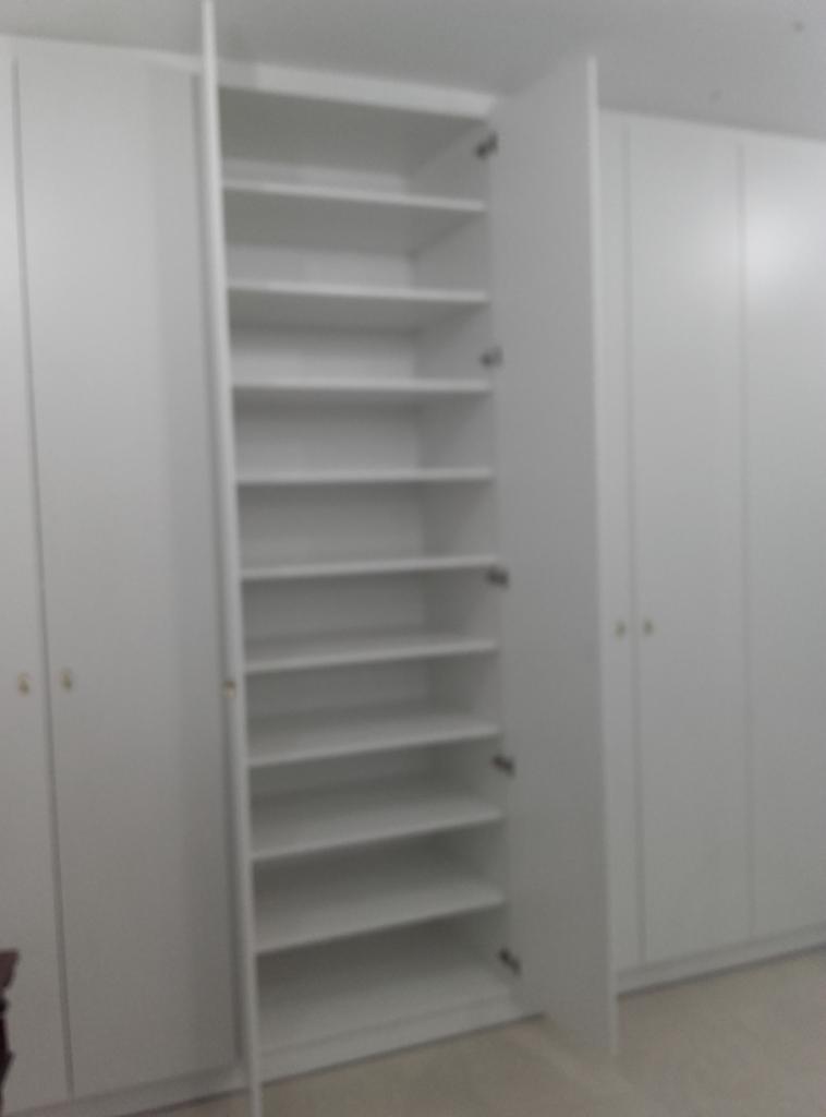 Wnętrze białej szafy wnękowej z otwartymi drzwiami, ukazującymi puste półki, na tle innych zamkniętych szaf o minimalistycznym designie.