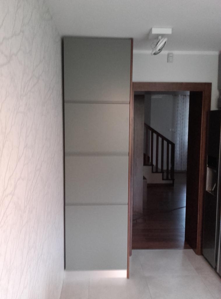 Wysoka, szara szafa wnękowa z delikatnym podświetleniem dolnej krawędzi, umieszczona w korytarzu z widokiem na schody.