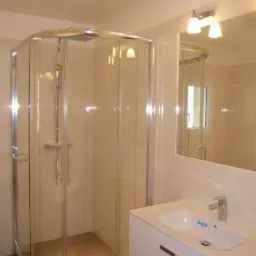 Jasna łazienka po remoncie: kabina prysznicowa z chromowanymi detalami, biała umywalka z szafką i lustro z oświetleniem. Minimalistyczny design.