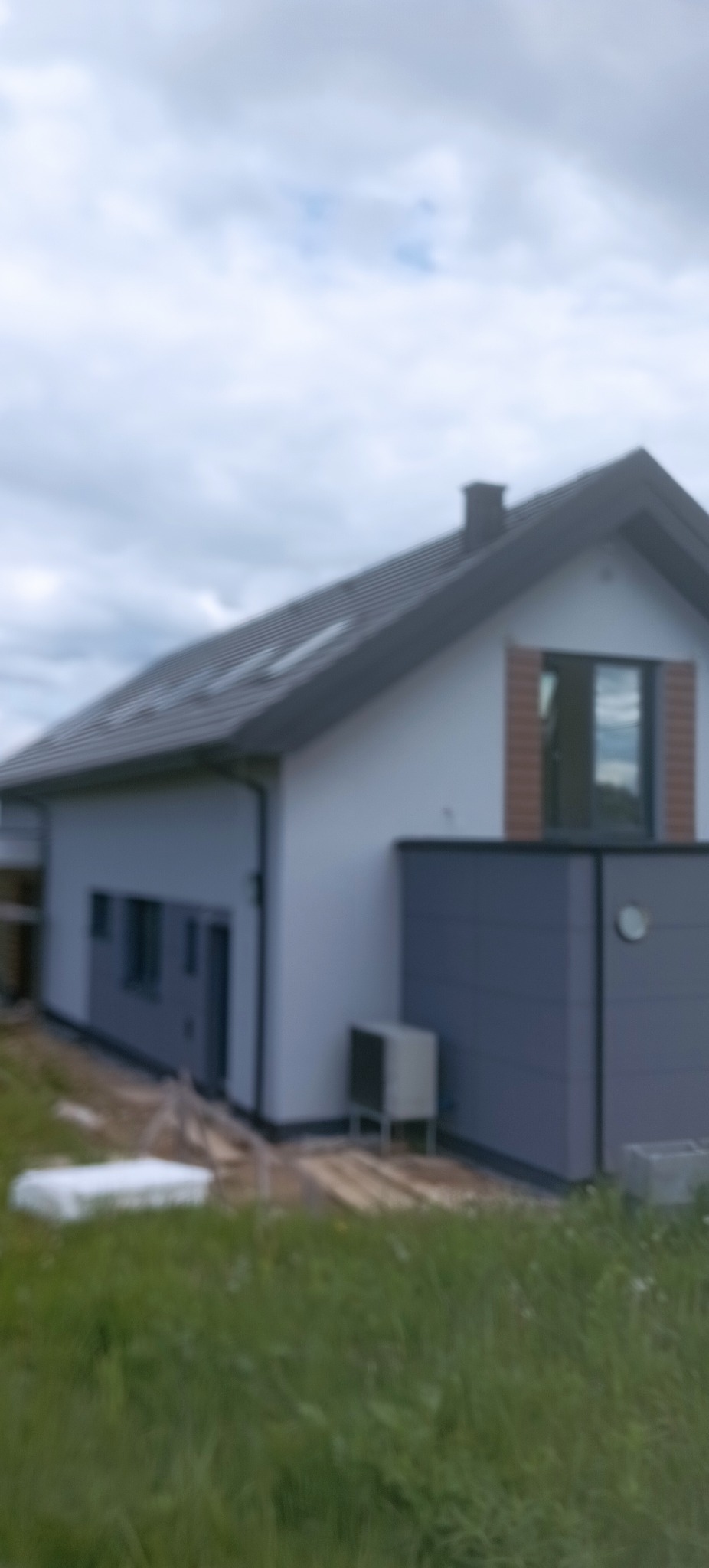 Nowoczesny dom jednorodzinny z jasną elewacją i grafitowymi akcentami, widoczny z perspektywy ogrodu. Elementy wykończeniowe z cegły przy oknie.