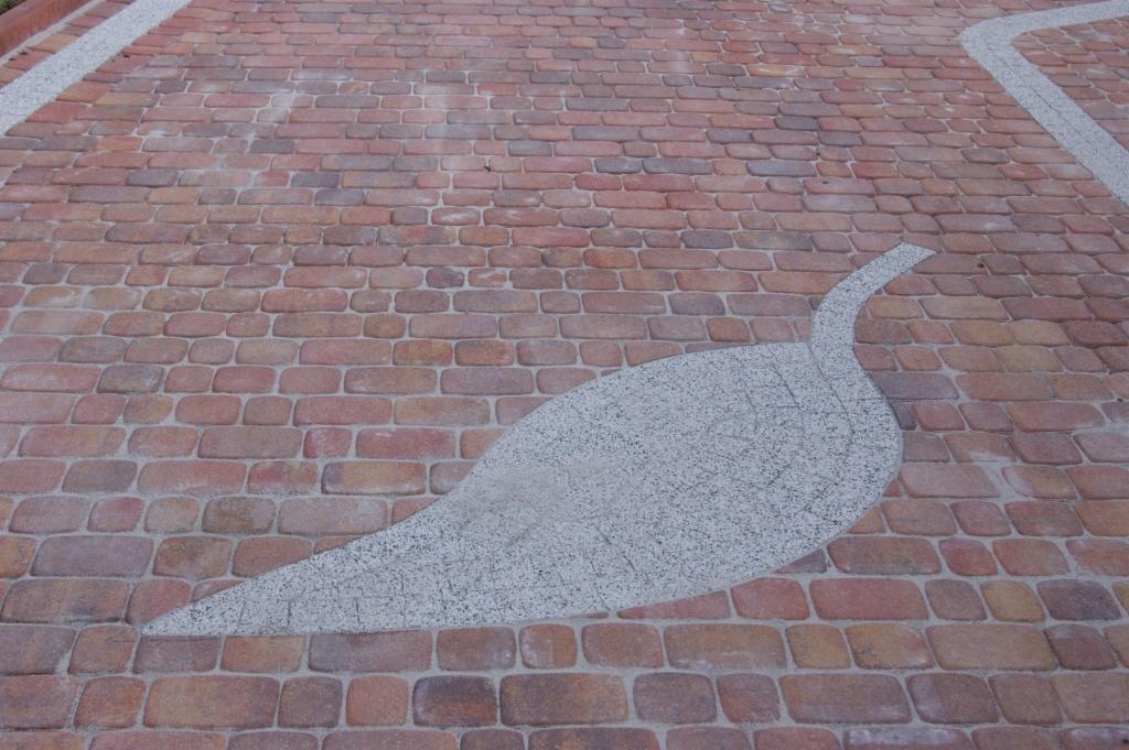 Chodnik z czerwonej kostki brukowej z dekoracyjnym motywem liścia wykonanym z szarego, drobnoziarnistego kamienia.