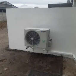 Zewnętrzna jednostka klimatyzacji marki York zamontowana na wspornikach do ściany budynku z widoczną instalacją odprowadzającą skropliny, grunt wokół częściowo wyłożony kostką.