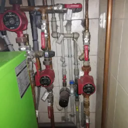 Rozbudowana instalacja grzewcza z kilkoma pompami obiegowymi Grundfos, zaworami Comap i manometrem ciśnienia w pomieszczeniu kotłowni w Chwaszczynie. Widoczne rury miedziane i plastikowe...