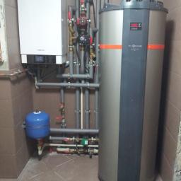 TWORKOWSKI S.C. - W kotłowni zainstalowany biały piec gazowy Viessmann obok szarego zbiornika na wodę Viessmann Vitocal 160 z pomarańczowymi akcentami, połączone szarymi rurami z zaworami.