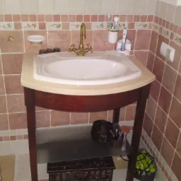 Umywalka nablatowa z baterią w stylu retro na drewnianym stelażu, z dekoracyjnymi płytkami na ścianie i akcesoriami łazienkowymi.