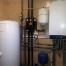 TWORKOWSKI S.C. - Kompaktowa kotłownia w beżowych płytkach, z białym zasobnikiem ciepłej wody, czarnym modułem sterującym z manometrami, białym naczyniem przeponowym i wiszącym kotłem gazowym Viessmann z wyświetlaczem.