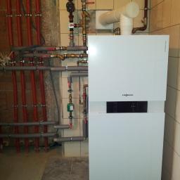 TWORKOWSKI S.C. - Nowoczesny, biały piec gazowy Viessmann z podłączeniami rur miedzianych i PCV, zamontowany na tle beżowych płytek ceramicznych. Widoczne liczne zawory i zabezpieczenia instalacji grzewczej.