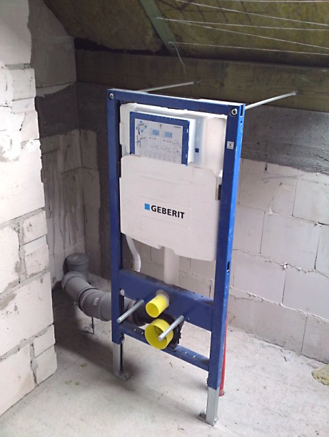 Stelaż podtynkowy Geberit w trakcie montażu w surowym wnętrzu, widoczne przyłącza kanalizacyjne i elementy mocujące do ściany z bloczków.