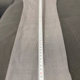 Przedsiębiorstwo Wielobranżowe „MONTEKS” Krzysztof Polański - Szare spodnie w kratę leżące na kanapie, mierzone białą miarką. Widoczny wzór kraty i numeracja na miarce.