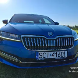 Niebieska Skoda Superb z przodu, zaparkowana na trawniku w słoneczny dzień, widoczna tablica rejestracyjna i logo Octavia Club.