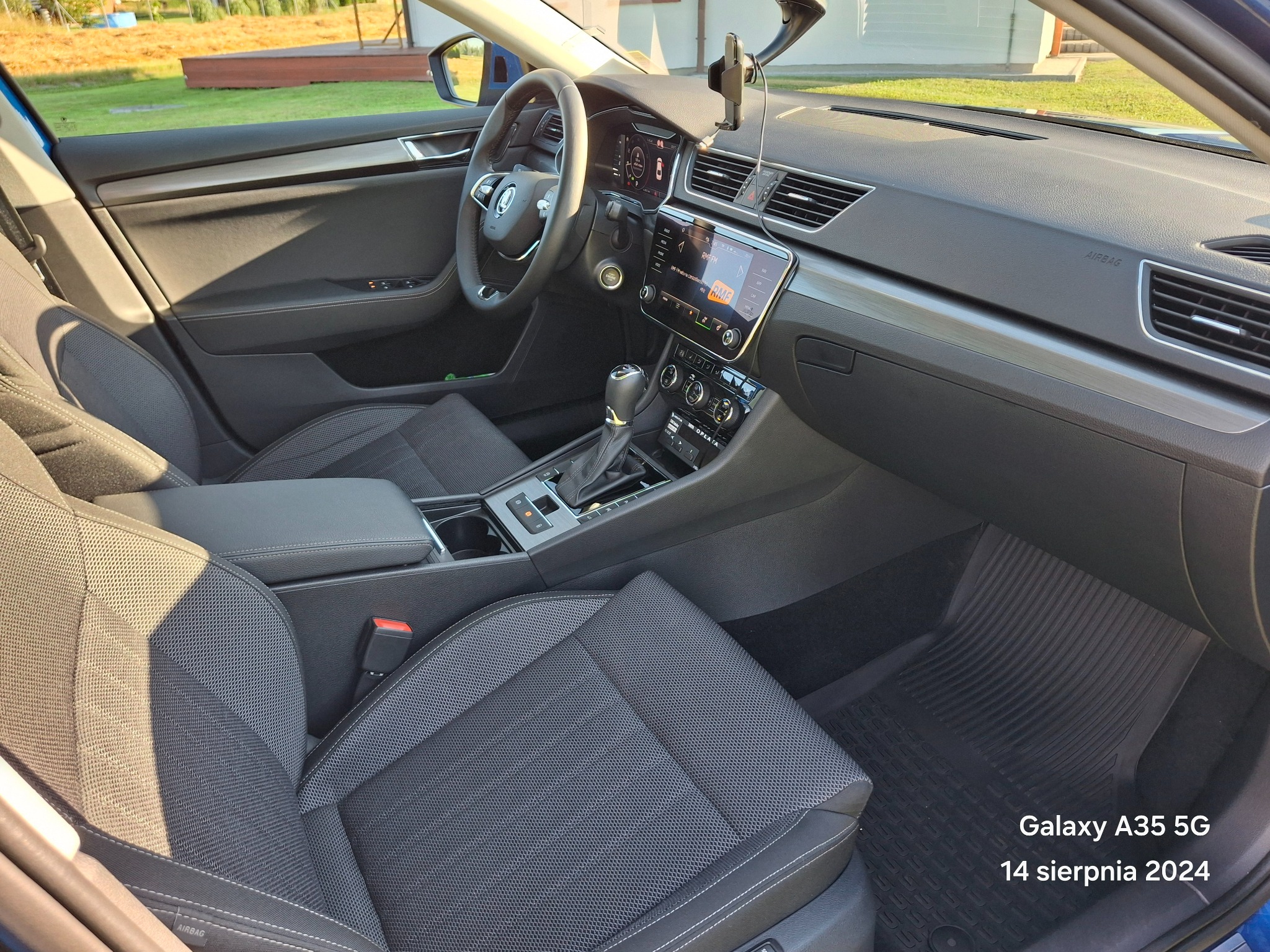 Wnętrze samochodu marki Skoda z widocznym kokpitem, kierownicą, fotelem kierowcy i konsolą środkową, z uchwytem na telefon przymocowanym do szyby.