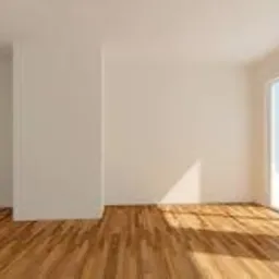 Puste, jasne pomieszczenie z parkietem w odcieniach brązu, białe ściany i duże okno balkonowe z widokiem na błękitne niebo, promienie słoneczne padające na podłogę.